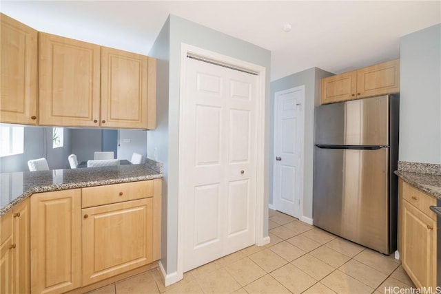 kitchen with stone countertops, stainless steel fridge, light brown cabinetry, and light tile patterned floors