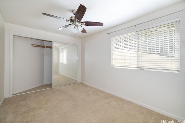 unfurnished bedroom featuring multiple windows, light colored carpet, ceiling fan, and a closet