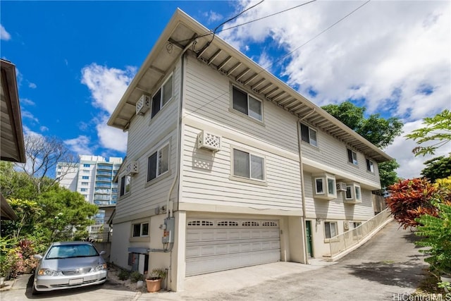 view of side of property with concrete driveway, an AC wall unit, and a garage