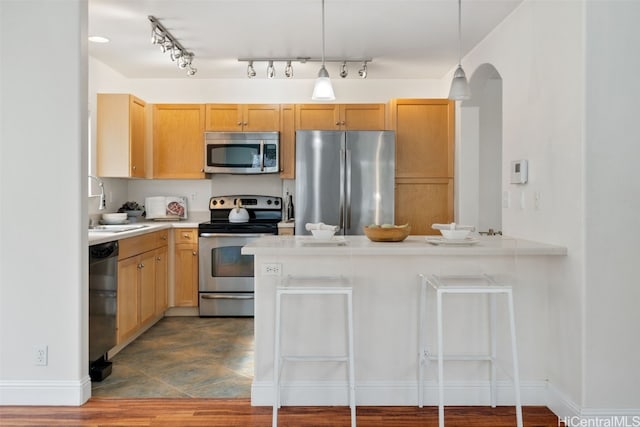 kitchen featuring kitchen peninsula, appliances with stainless steel finishes, light brown cabinetry, sink, and decorative light fixtures