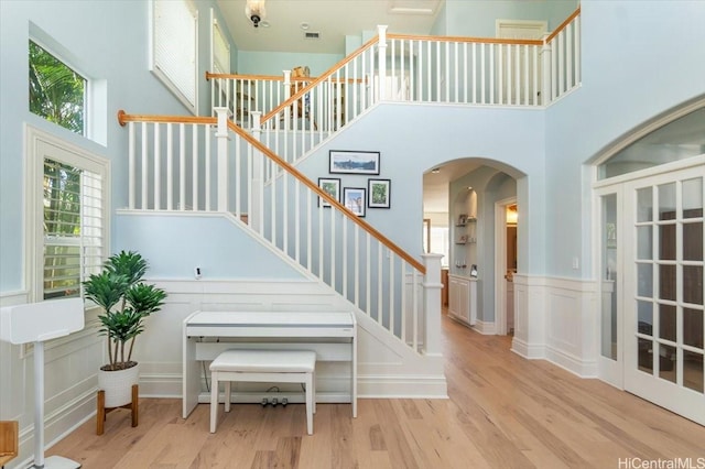 staircase with a towering ceiling, arched walkways, a wealth of natural light, and wood finished floors