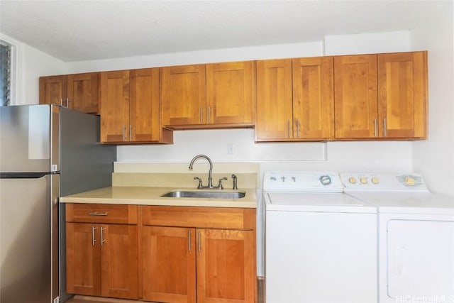 kitchen featuring brown cabinetry, freestanding refrigerator, light countertops, separate washer and dryer, and a sink