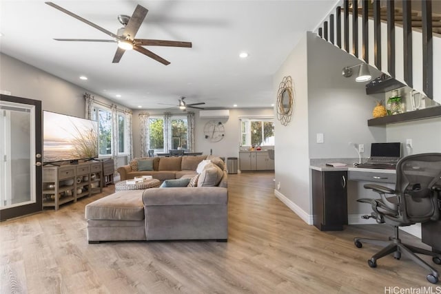 living room with light wood-type flooring, a wall unit AC, and ceiling fan