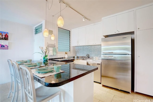 kitchen featuring hanging light fixtures, a kitchen breakfast bar, backsplash, white cabinets, and appliances with stainless steel finishes