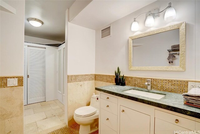 bathroom featuring vanity, tile walls, and toilet