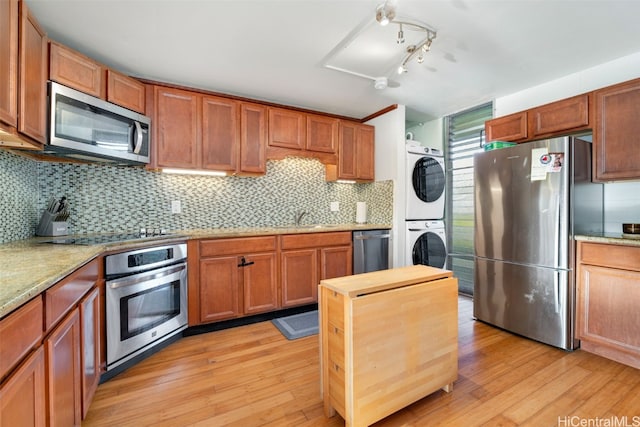 kitchen featuring stacked washer / drying machine, tasteful backsplash, light stone counters, light wood-type flooring, and appliances with stainless steel finishes