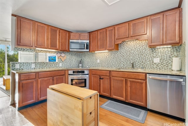 kitchen with appliances with stainless steel finishes, sink, light wood-type flooring, and decorative backsplash