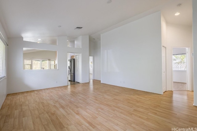 spare room with a healthy amount of sunlight, light wood-type flooring, and high vaulted ceiling