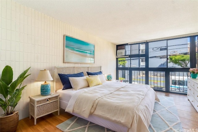 bedroom with a wall of windows, a textured ceiling, and light hardwood / wood-style flooring