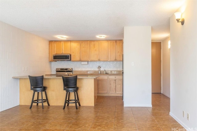 kitchen with a kitchen breakfast bar, a textured ceiling, appliances with stainless steel finishes, tasteful backsplash, and kitchen peninsula