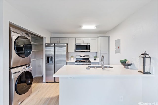 kitchen with kitchen peninsula, stacked washing maching and dryer, tasteful backsplash, stainless steel appliances, and sink