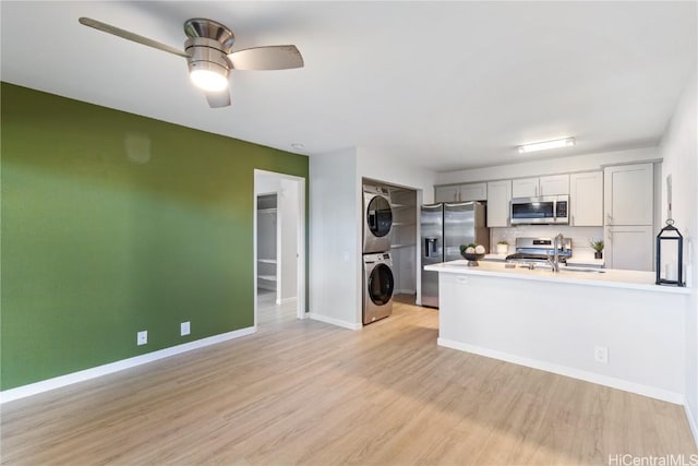 kitchen with ceiling fan, stacked washer and dryer, decorative backsplash, appliances with stainless steel finishes, and light wood-type flooring