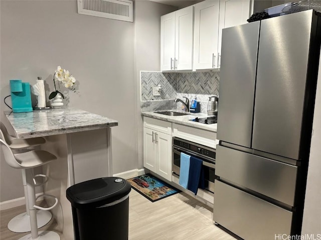 kitchen featuring white cabinetry, sink, light stone counters, backsplash, and appliances with stainless steel finishes