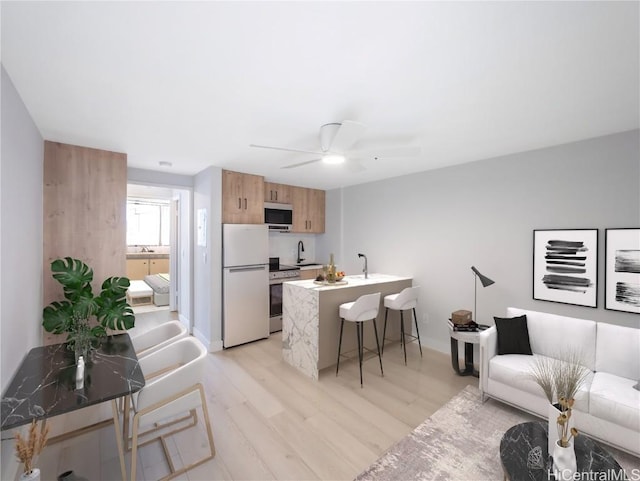 kitchen with ceiling fan, sink, stainless steel appliances, a kitchen breakfast bar, and light hardwood / wood-style floors