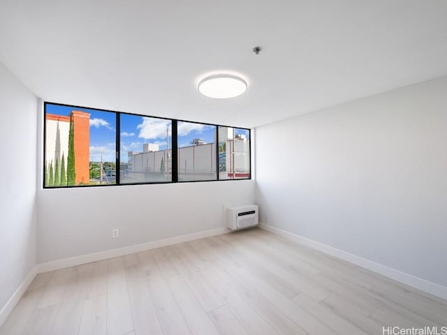 empty room with an AC wall unit and light wood-type flooring