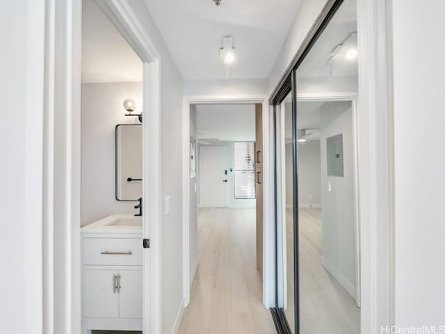 hall featuring electric panel, sink, and light wood-type flooring