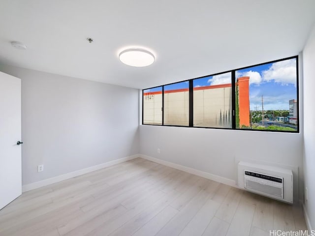 unfurnished room featuring light wood-type flooring, a wall unit AC, and a wealth of natural light