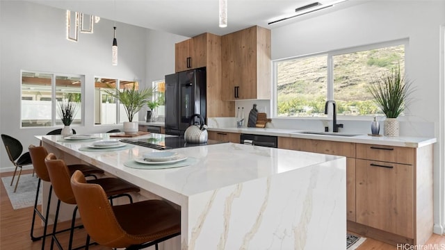 kitchen featuring light wood-type flooring, a breakfast bar, black appliances, decorative light fixtures, and a center island