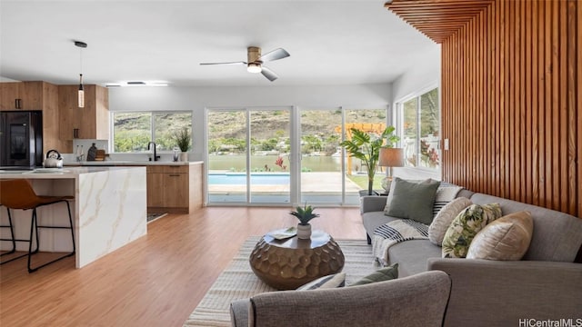 living room featuring plenty of natural light, light hardwood / wood-style floors, sink, and ceiling fan