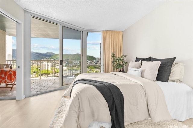 bedroom featuring hardwood / wood-style floors, a mountain view, access to outside, expansive windows, and a textured ceiling