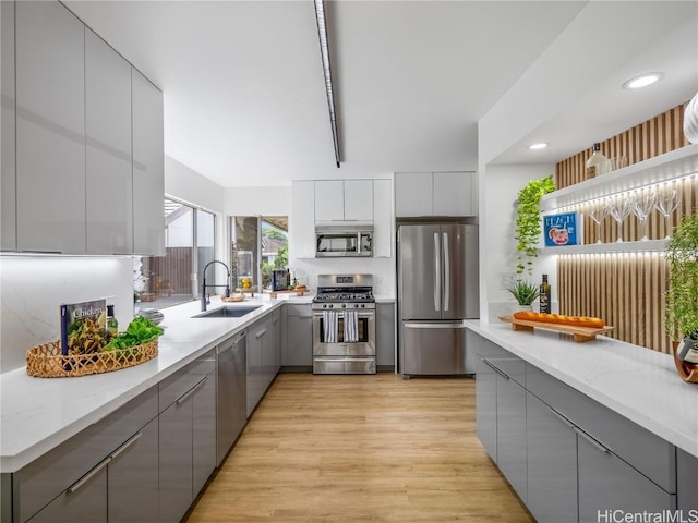 kitchen with gray cabinetry, sink, light hardwood / wood-style floors, and appliances with stainless steel finishes