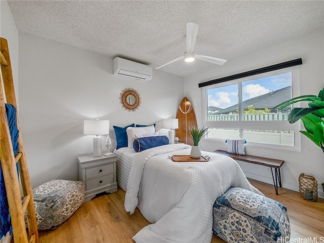 bedroom with an AC wall unit, ceiling fan, light hardwood / wood-style flooring, and a textured ceiling