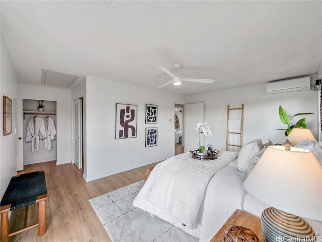 bedroom with a wall mounted AC, ceiling fan, a textured ceiling, and light wood-type flooring