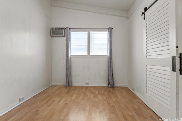 spare room with light hardwood / wood-style floors, a wall unit AC, and a barn door