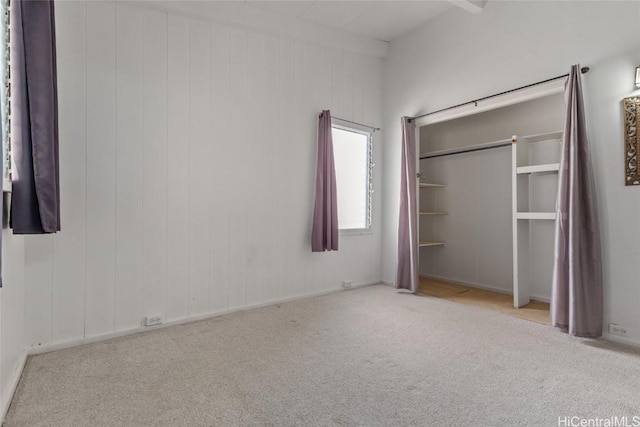 unfurnished bedroom with a closet, wood walls, and light carpet