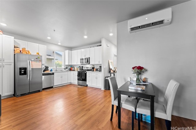 kitchen featuring white cabinets, stainless steel appliances, a wall unit AC, and light hardwood / wood-style flooring