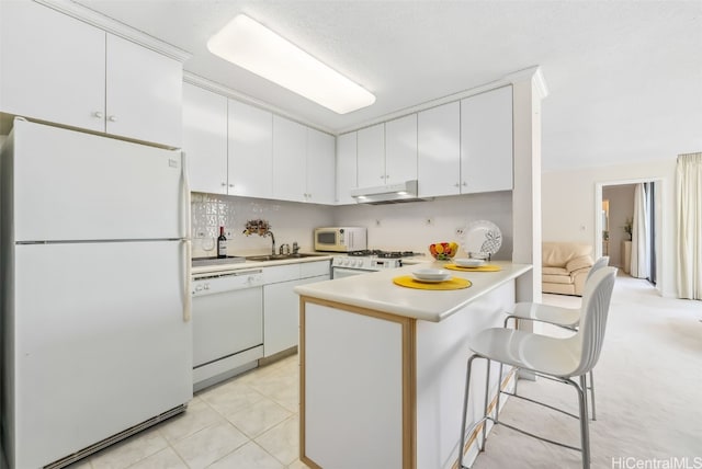 kitchen with a breakfast bar, white appliances, white cabinets, light tile patterned floors, and kitchen peninsula