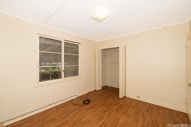 unfurnished bedroom with wood-type flooring, wood walls, and a closet