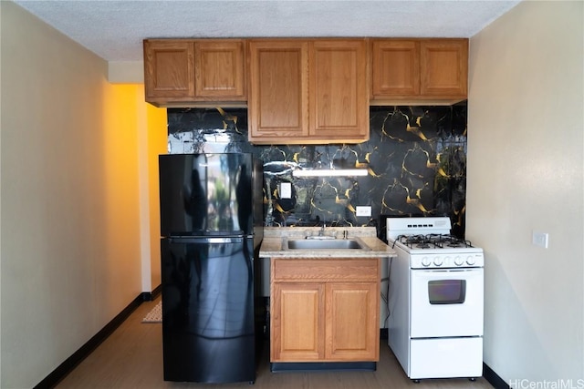 kitchen featuring a textured ceiling, black refrigerator, sink, backsplash, and white gas stove