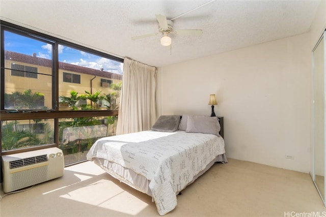 bedroom featuring floor to ceiling windows, light colored carpet, a wall unit AC, and ceiling fan