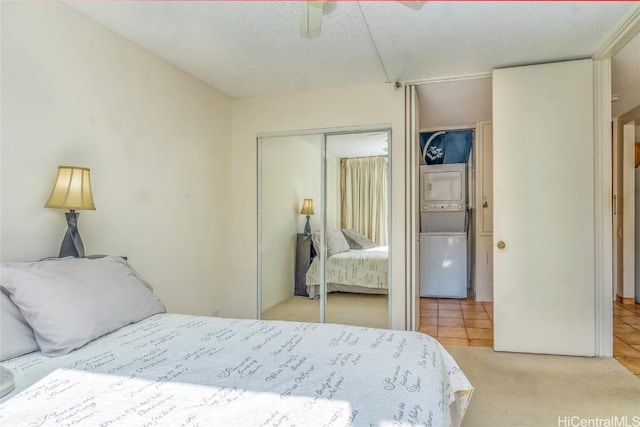 bedroom with a textured ceiling, ceiling fan, light tile patterned floors, a closet, and stacked washer and dryer