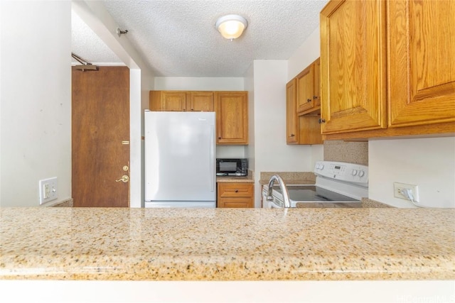 kitchen featuring white appliances, a textured ceiling, and light stone counters