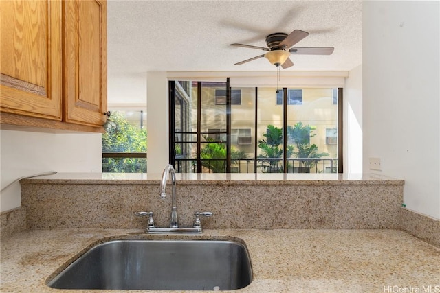 kitchen featuring sink, a textured ceiling, ceiling fan, and light stone counters