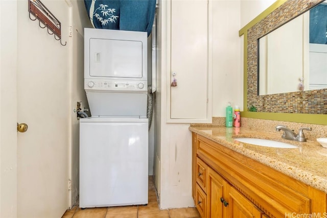 laundry room featuring stacked washer and dryer, light tile patterned floors, and sink