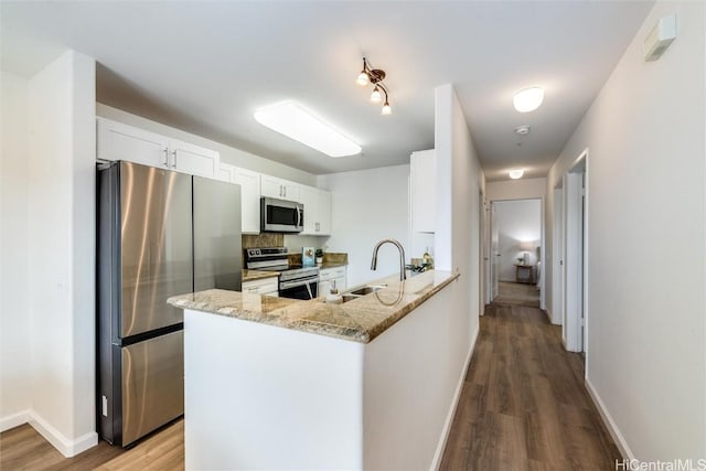 kitchen with sink, white cabinetry, stainless steel appliances, light stone countertops, and kitchen peninsula