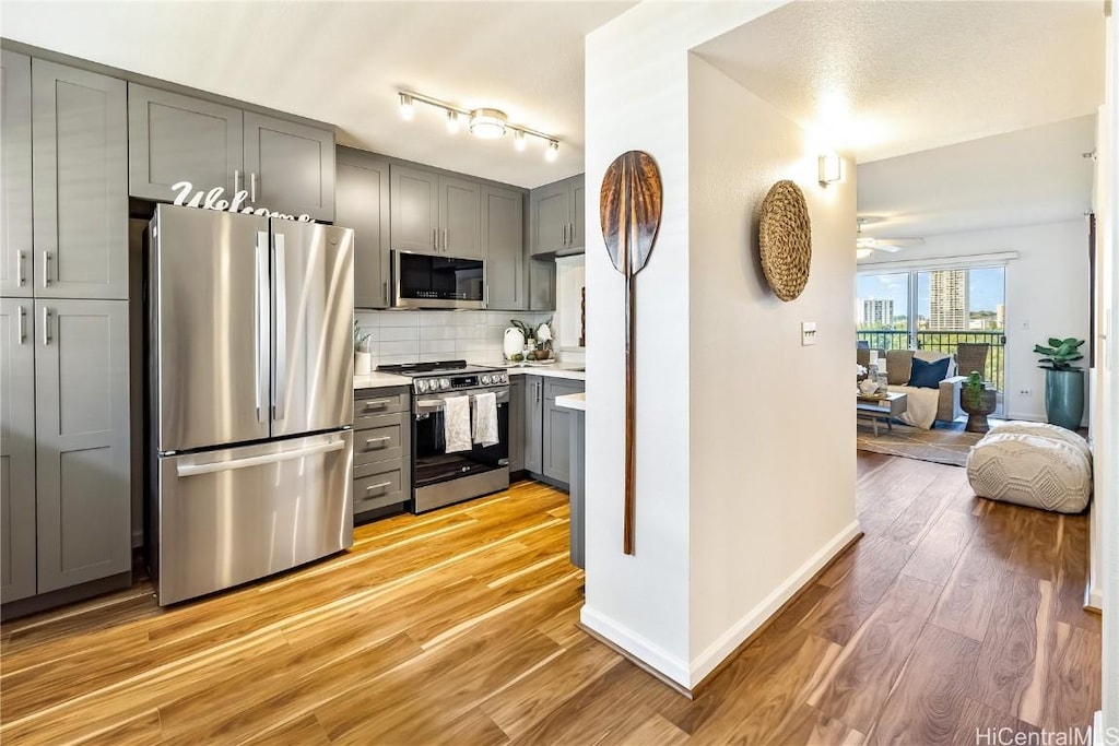 kitchen featuring backsplash, stainless steel appliances, gray cabinets, and light hardwood / wood-style floors