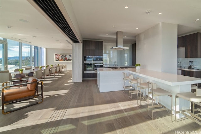 kitchen with floor to ceiling windows, kitchen peninsula, island exhaust hood, light hardwood / wood-style flooring, and dark brown cabinetry