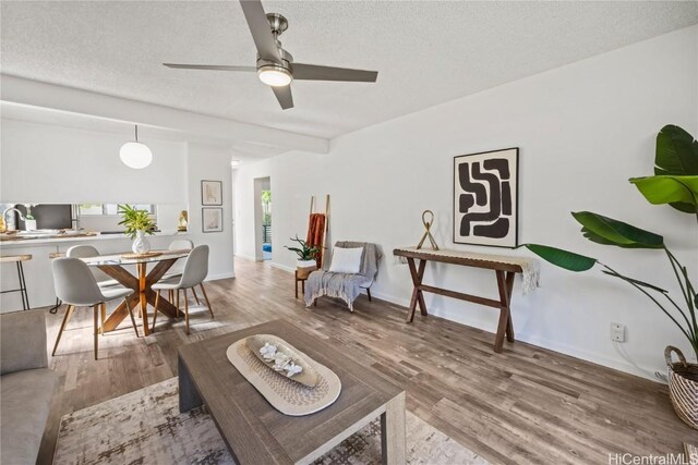 living room with a textured ceiling, ceiling fan, hardwood / wood-style floors, and beamed ceiling