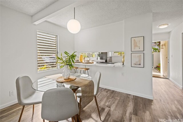 dining room featuring a textured ceiling, hardwood / wood-style floors, plenty of natural light, and beam ceiling