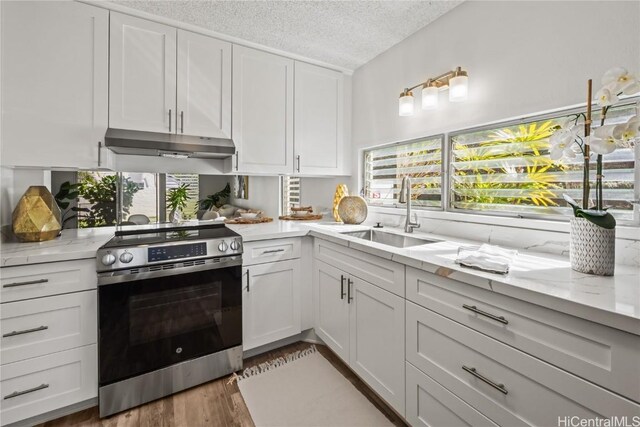 kitchen with light stone counters, a textured ceiling, stainless steel range with electric cooktop, white cabinets, and sink