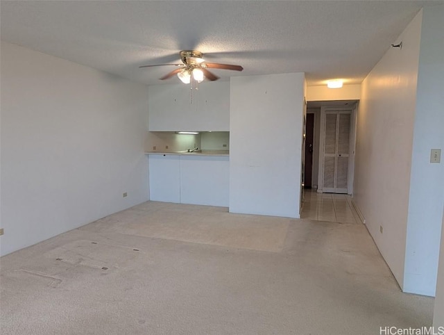 unfurnished living room featuring ceiling fan, light colored carpet, and a textured ceiling