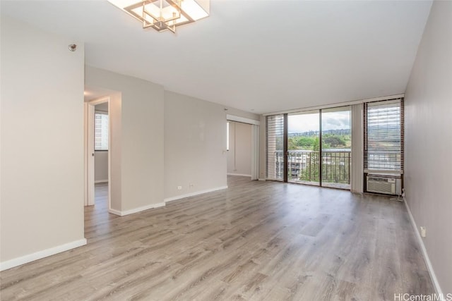 empty room featuring floor to ceiling windows, cooling unit, a chandelier, and light wood-type flooring