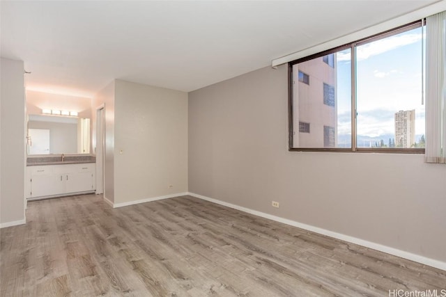 unfurnished bedroom featuring light hardwood / wood-style floors, sink, connected bathroom, and multiple windows