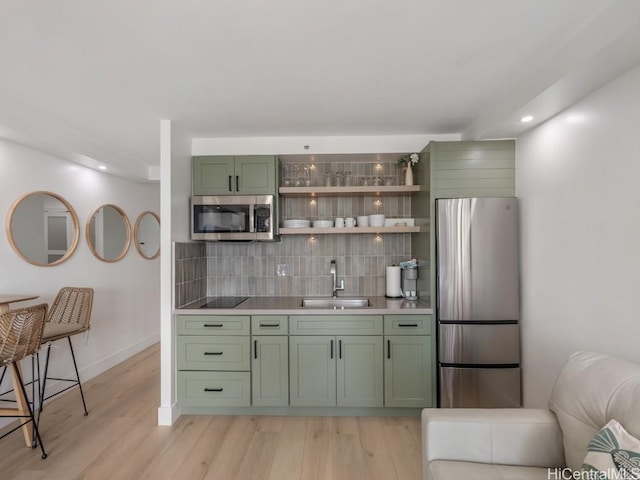 bar with sink, light hardwood / wood-style flooring, decorative backsplash, appliances with stainless steel finishes, and green cabinetry