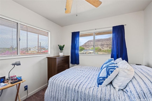 bedroom featuring a mountain view, ceiling fan, carpet flooring, and multiple windows