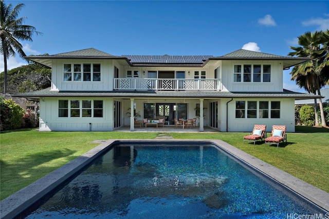 rear view of property with a balcony, a lawn, and solar panels